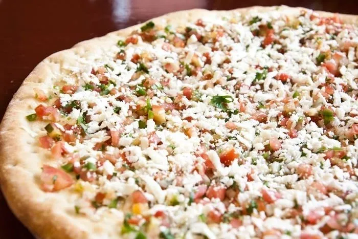 A pizza with tomatoes and cheese on top of a wooden table.