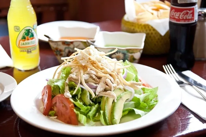 A plate of chicken salad on a table next to a bottle of coca cola.